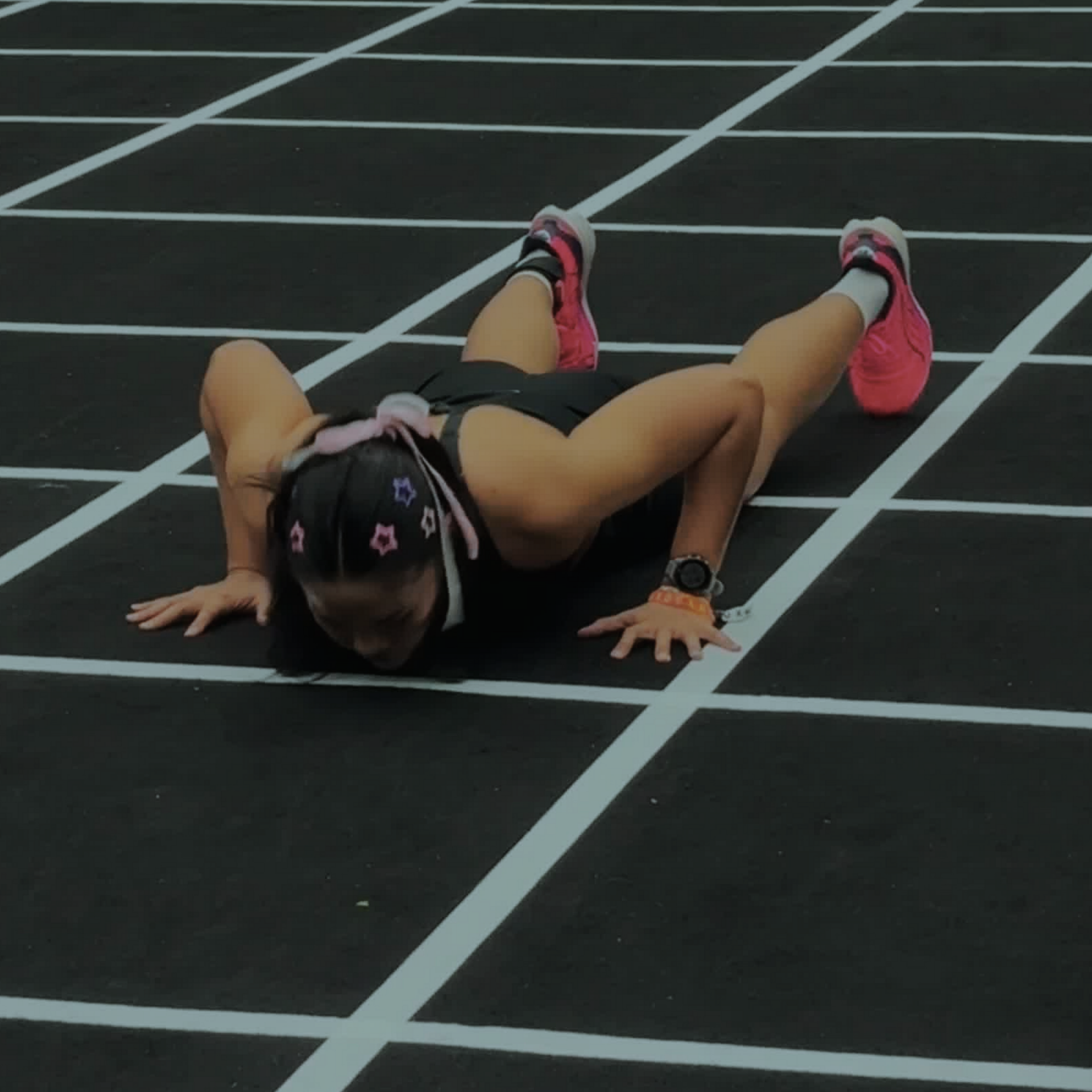 Athlete lying face down on a track, arms outstretched, wearing black and pink running shoes