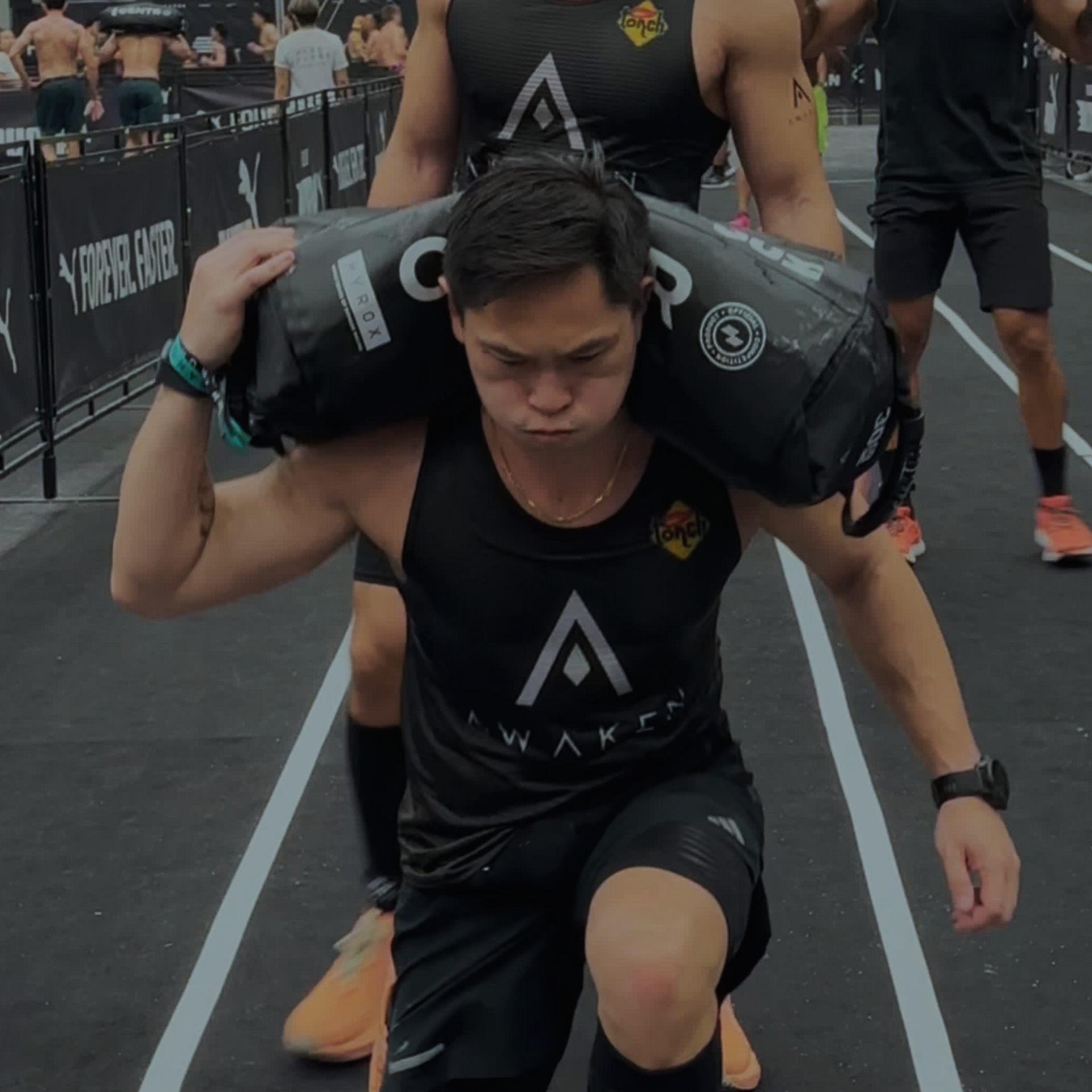 Athlete lunges forward carrying a black sandbag on shoulders during an outdoor obstacle race