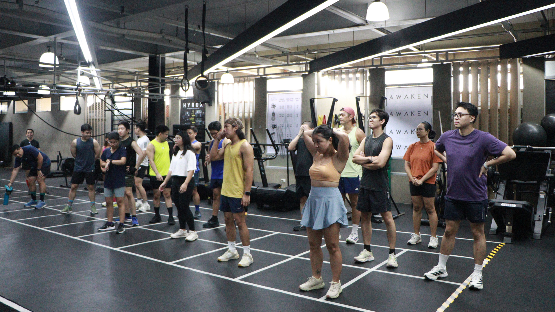Group fitness class in a gym, with people standing on marked floor squares exercising in rows