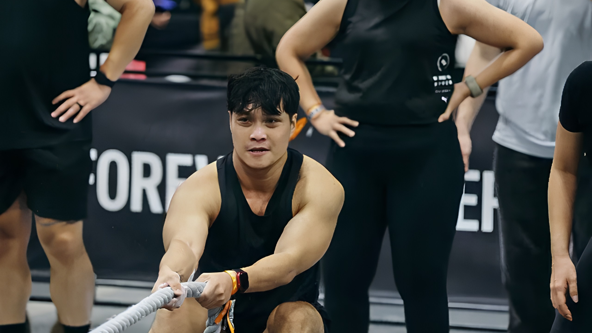 Athlete performing a sandbag lunges in a HYROX competition, with a partner watching behind.