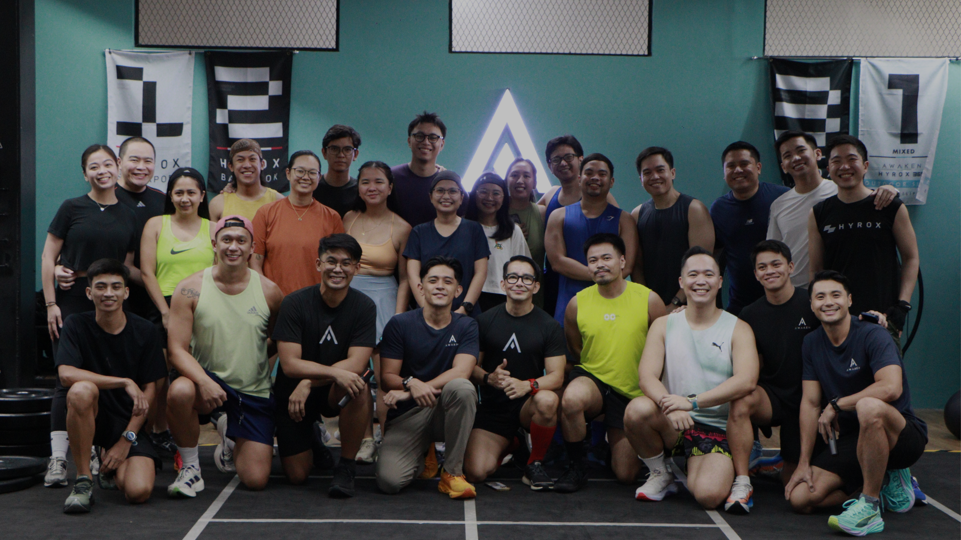 Group of people posing in a gym, some standing and some kneeling, in front of exercise equipment.