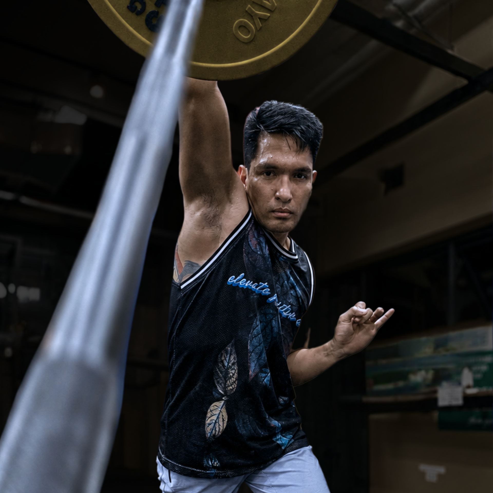 Weightlifter in a black tank top raises one arm under a barbell plate in a dim gym