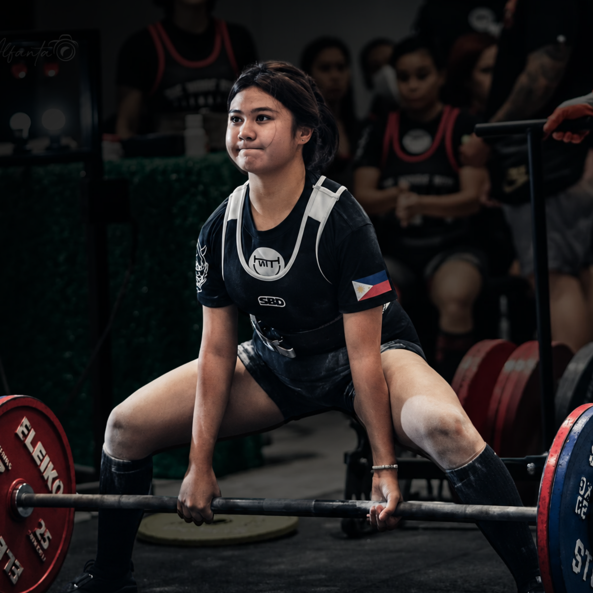 Smiling athlete in black tank top flexing and giving thumbs up against a dark sponsor backdrop