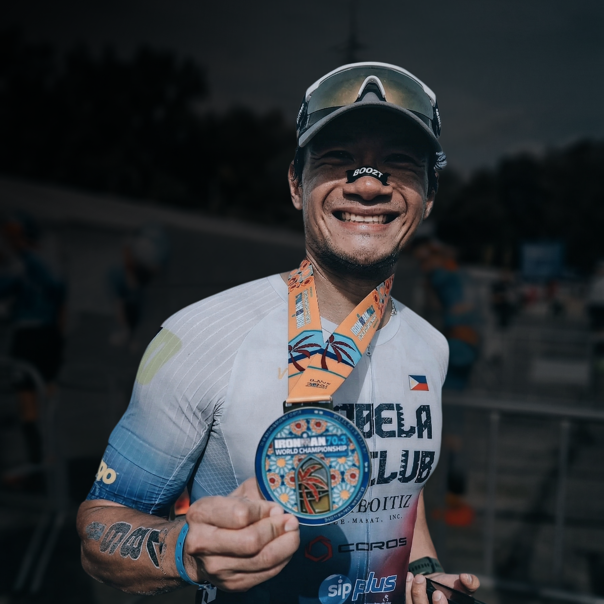 Smiling runner holding a finisher medal, wearing a cap and white shirt outdoors at a race event