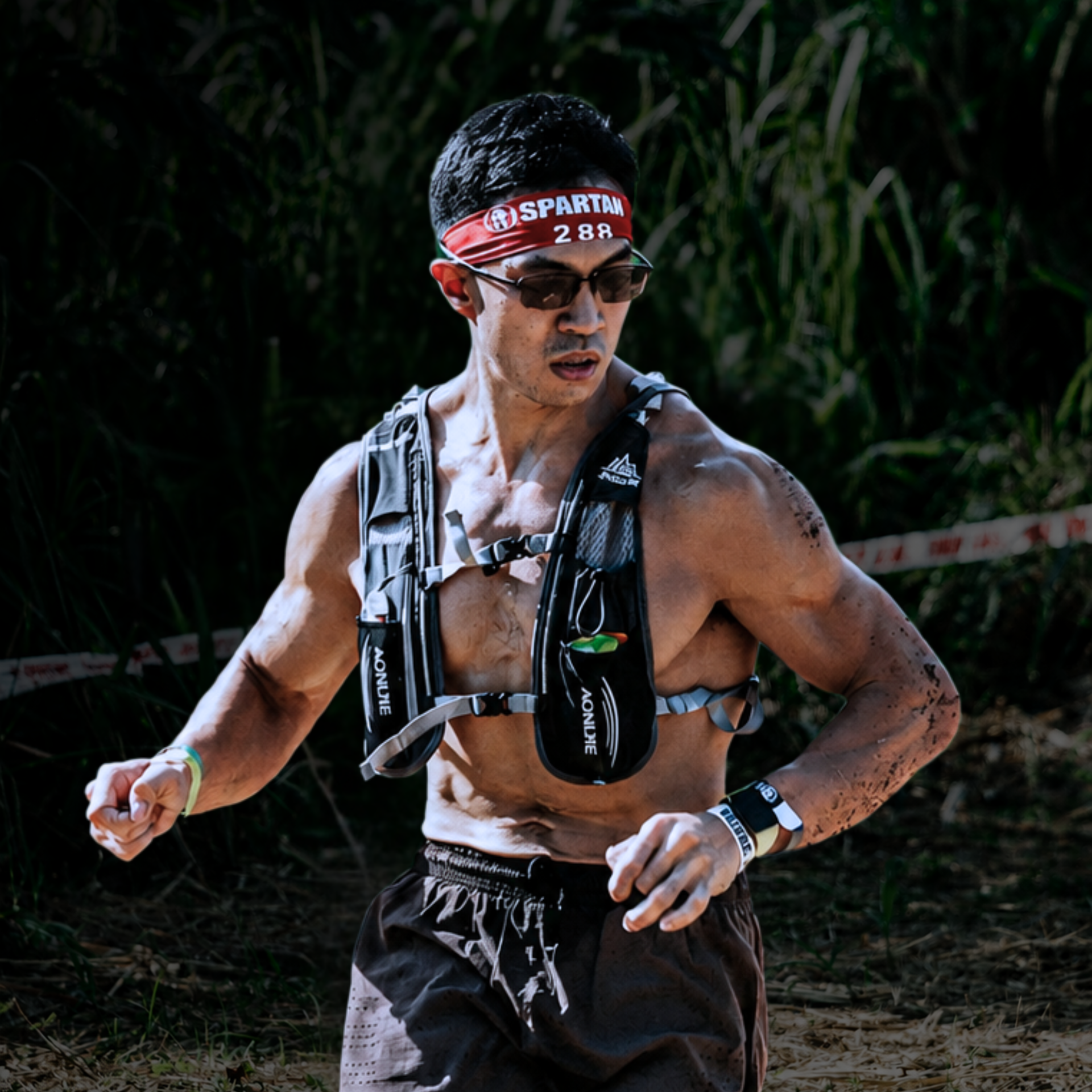 Runner wearing a headband and hydration vest, mid-stride on a muddy trail with water spray
