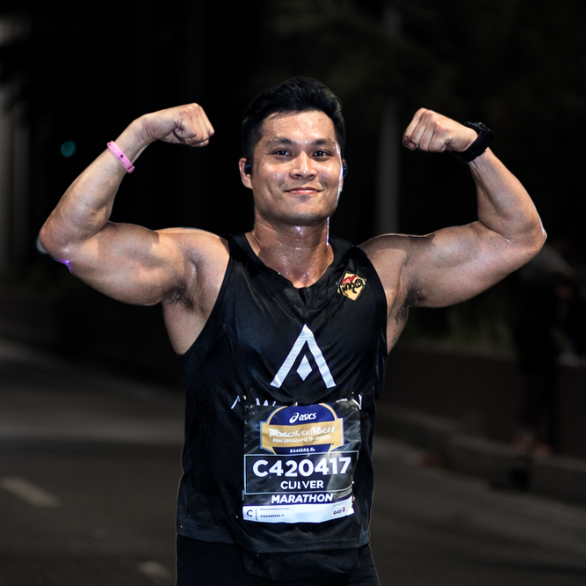 Athlete in black tank top flexing both arms and smiling after a race, wearing a bib number.