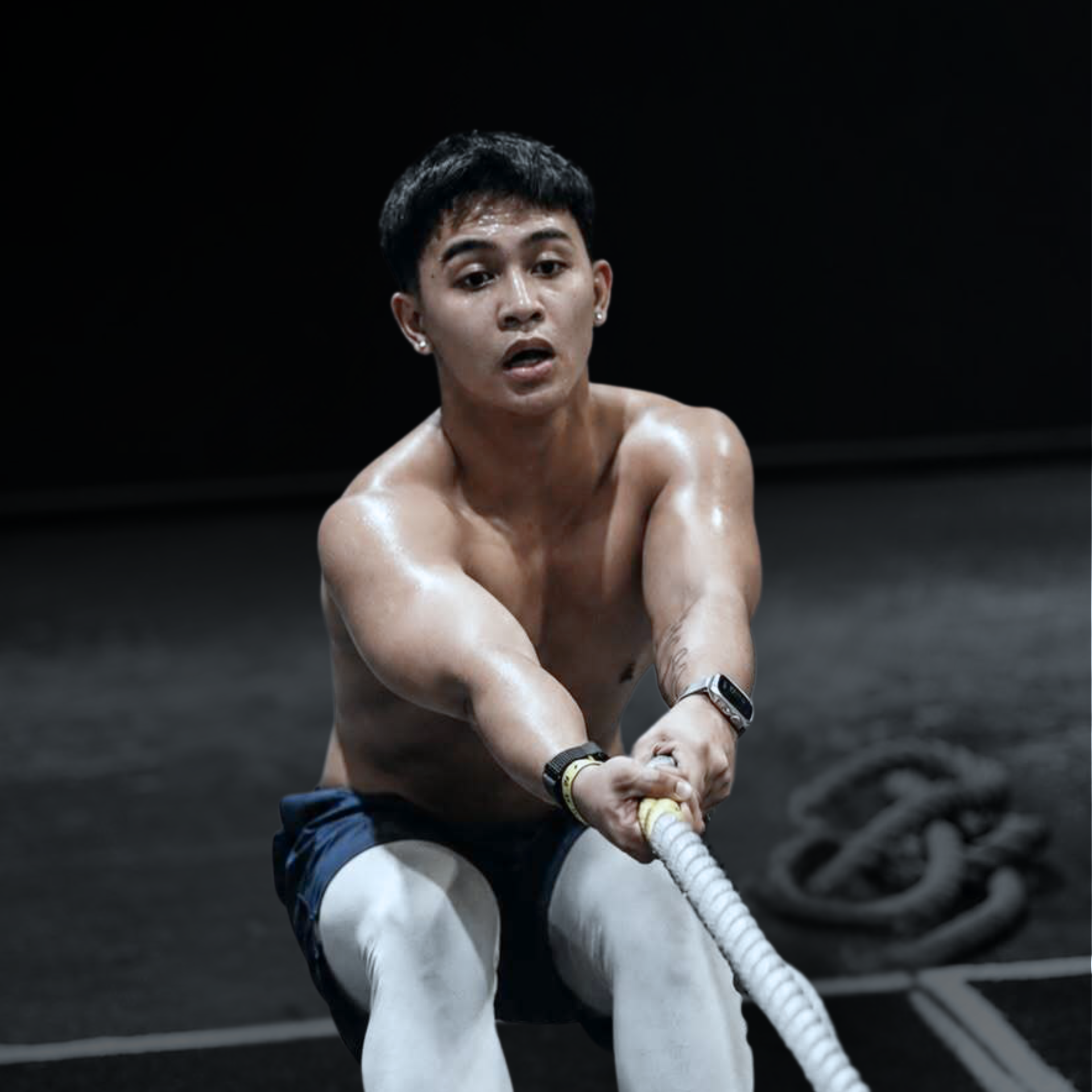 Athlete pulling battle ropes in a dark gym, focused and sweating.