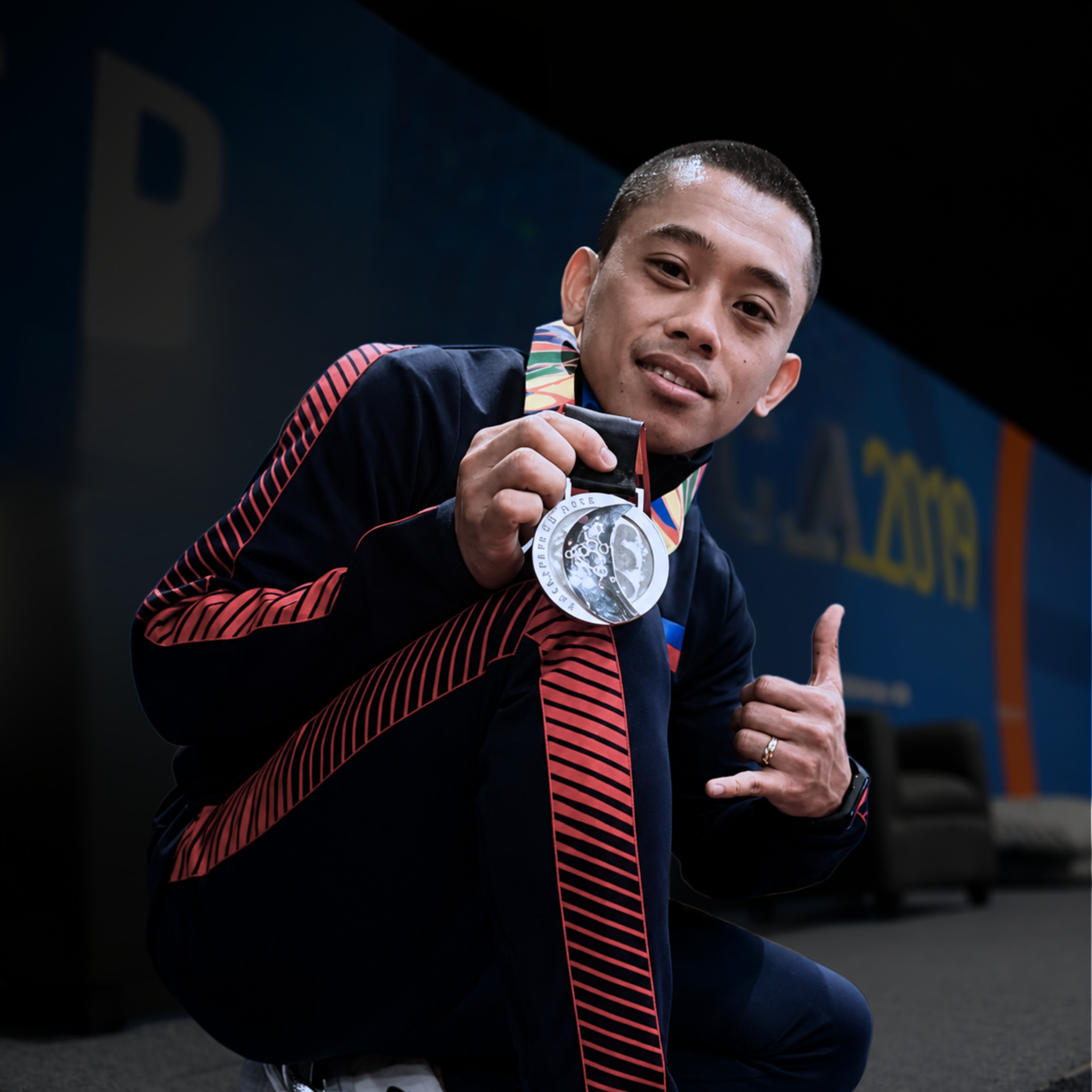 Athlete holding up a silver medal and giving a thumbs-up on a stage