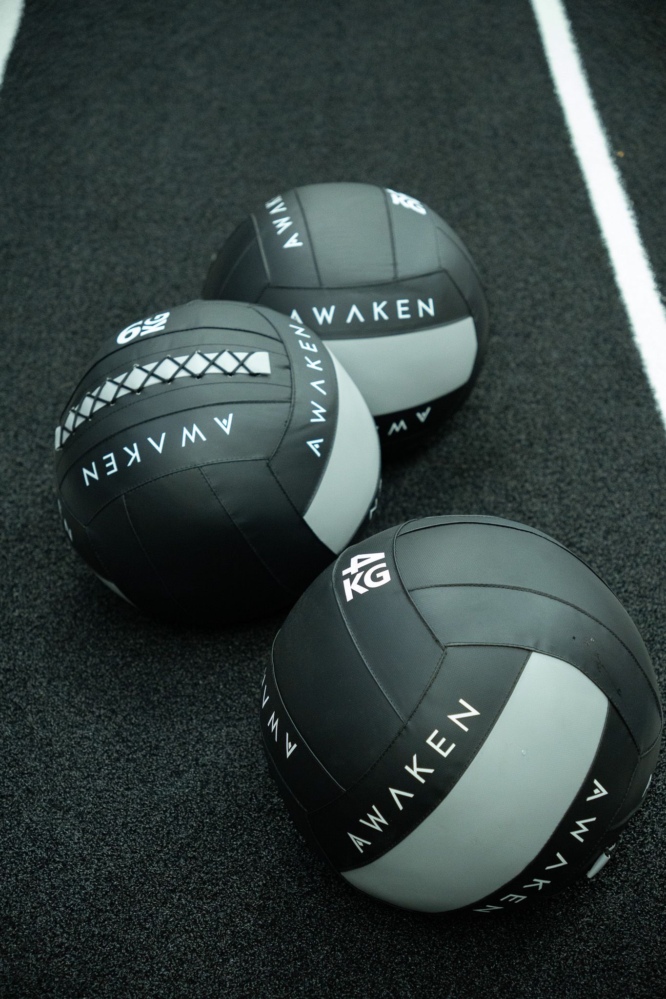 Three black and gray medicine balls on a gym floor, each labeled “AWAKEN.”