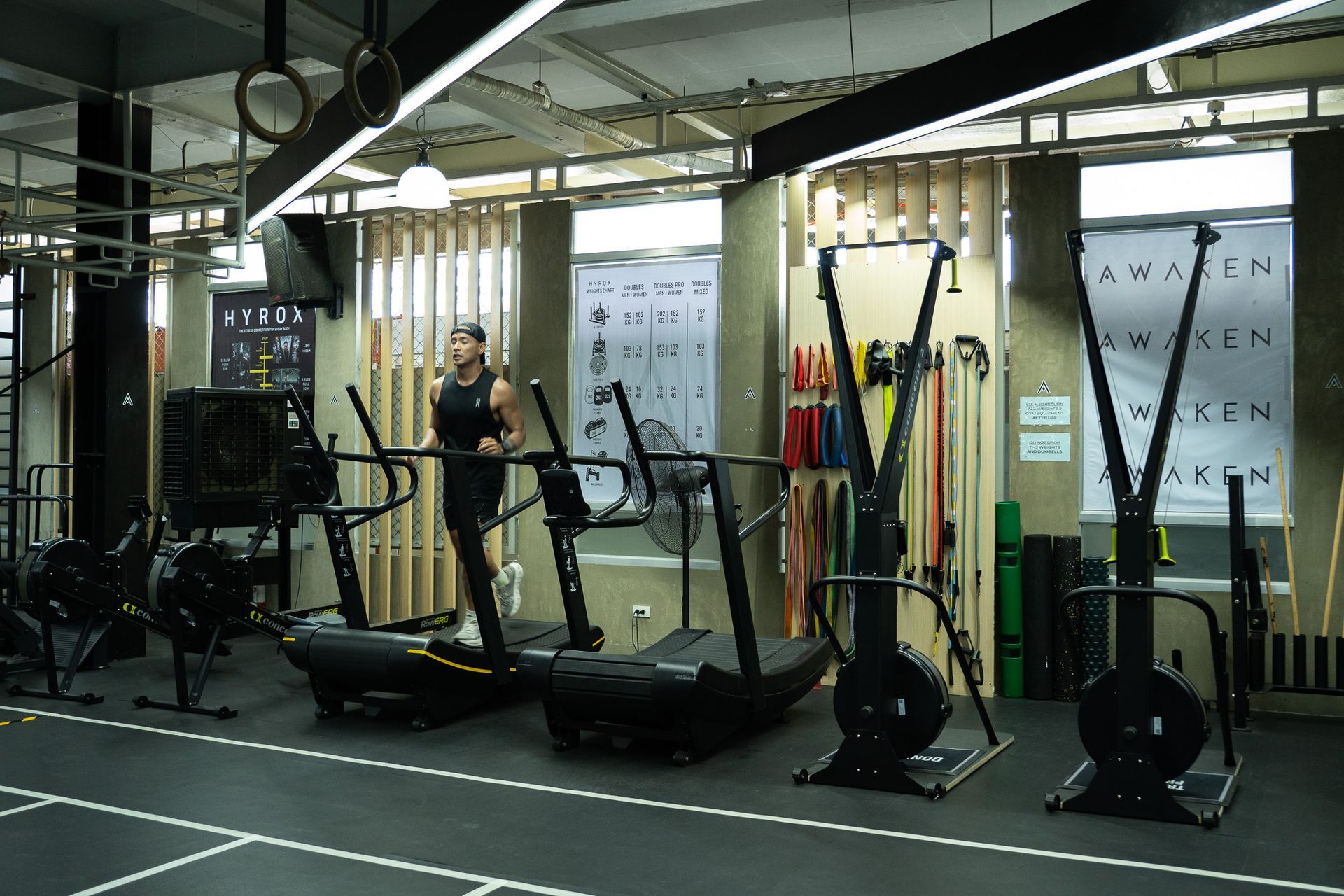 Three people in a gym setting, with two standing and one seated on a weight bench, engaged in conversation.