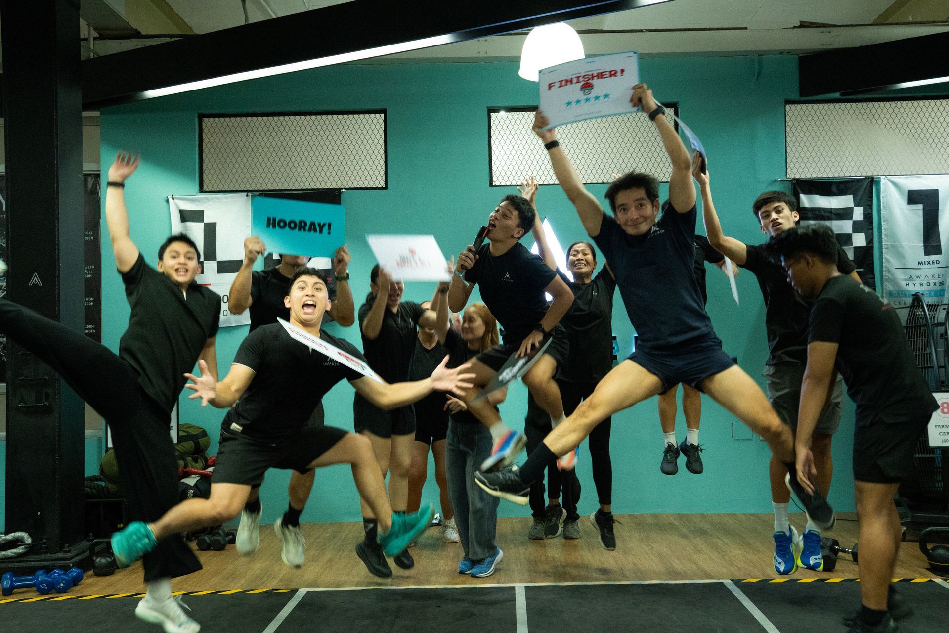 A large group of people posing for a photo on a stage at a Hyrox competition with black banners in the background.