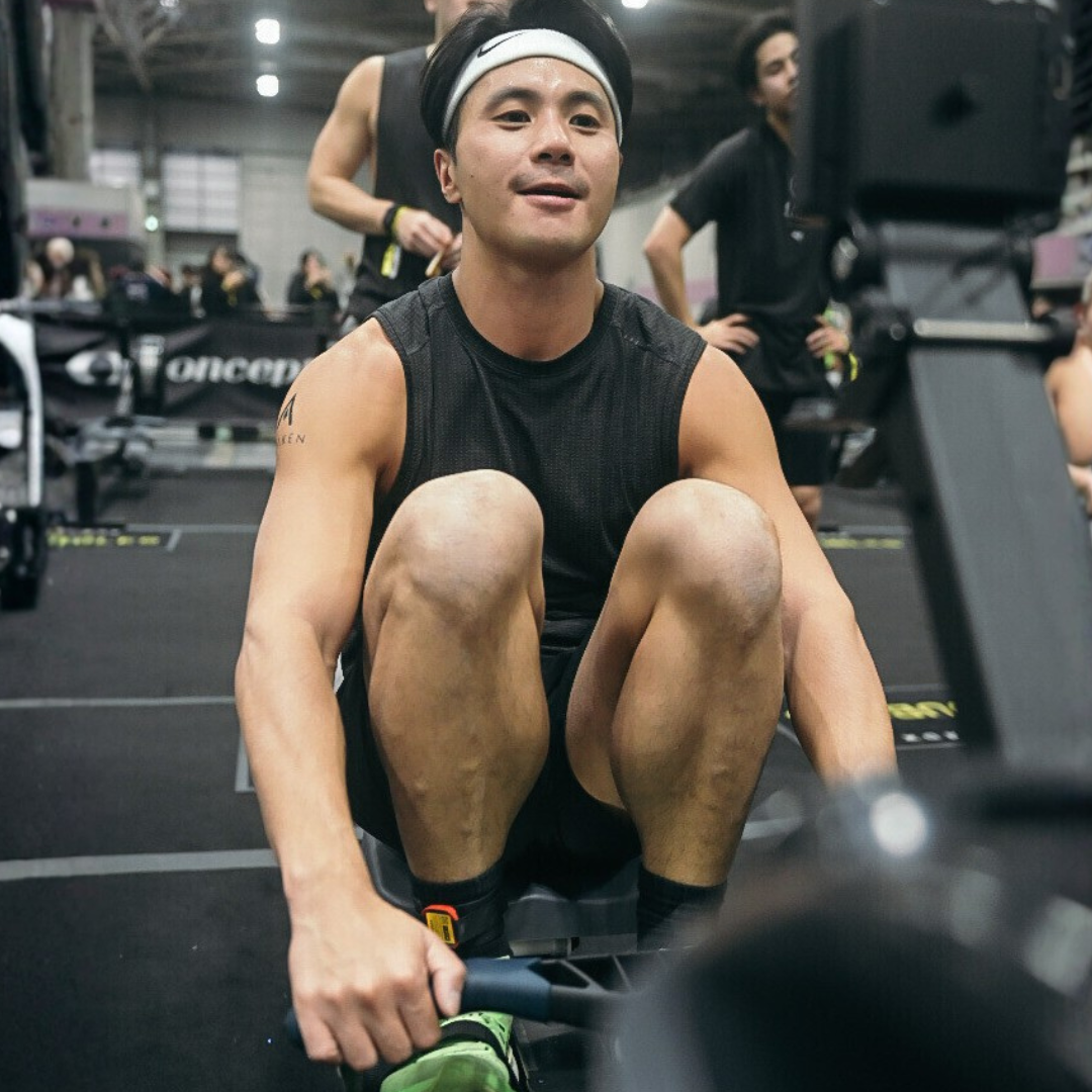 Man exercising on a rowing machine in a gym, wearing a black sleeveless top and headband.