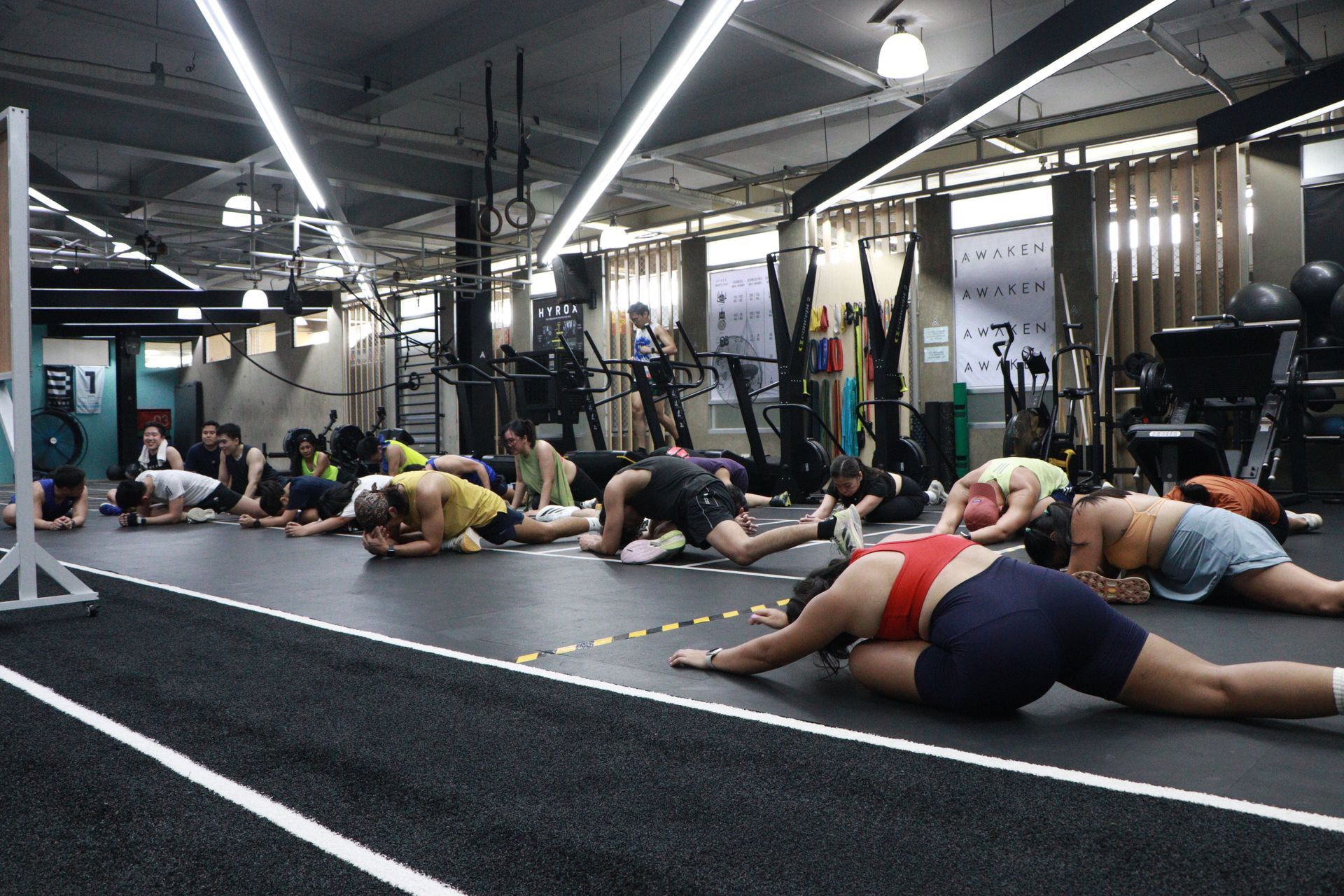 People practice yoga in a gym, holding a high lunge pose with arms raised on individual mats over artificial turf.
