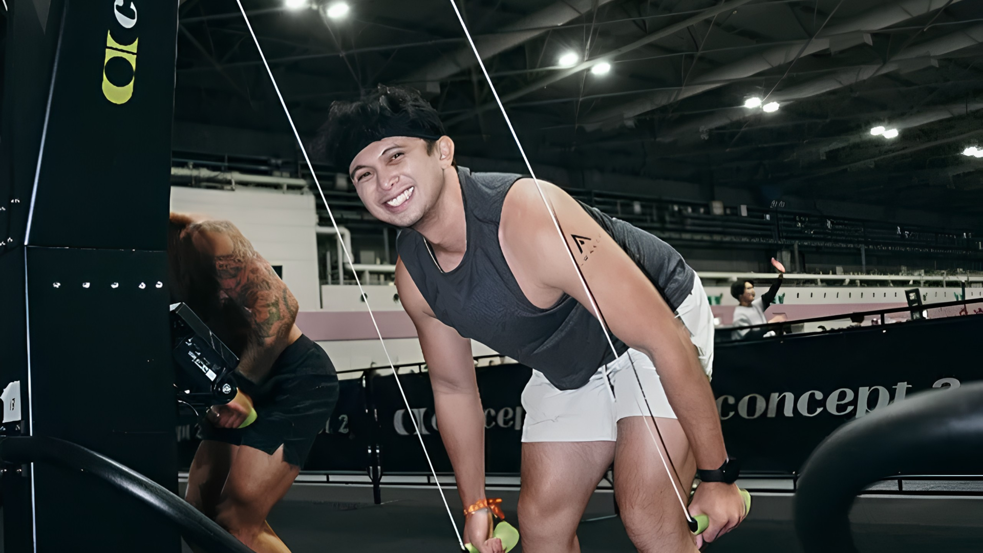 Woman smiling and leaning forward in a gym, holding ropes near exercise equipment.
