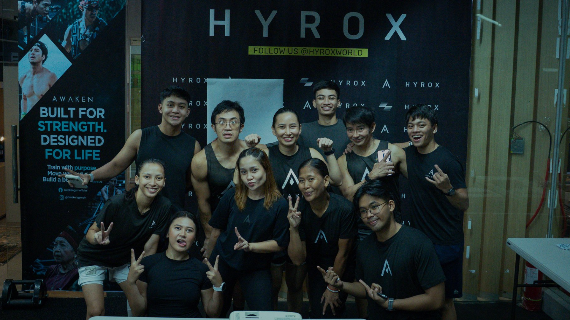 Group of athletes posing in front of a HYROX banner at an indoor event booth.