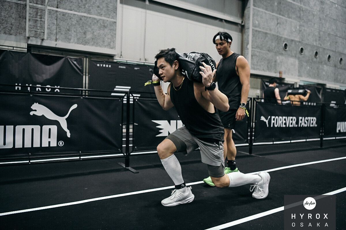 Two runners sprint side by side on a track, wearing black gear in an indoor stadium.
