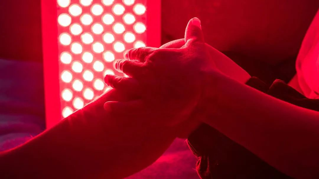 Hands positioned in front of a panel emitting bright red therapeutic light.