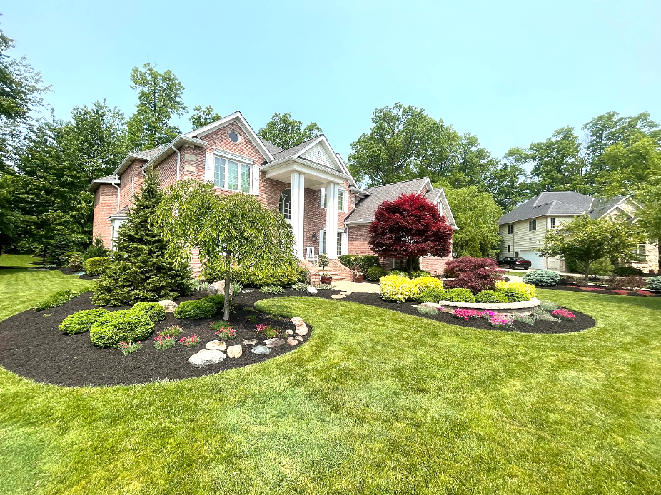 A two-story brick house with white columns and a well-landscaped yard under a blue sky.