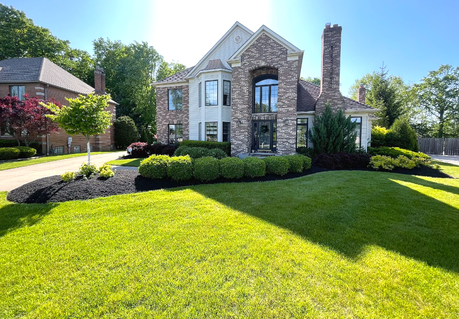 Two-story house with stone facade, dark green door, and manicured lawn on a sunny day.
