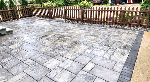 Patio paved with gray blocks, framed by a brown picket fence and a dark border.