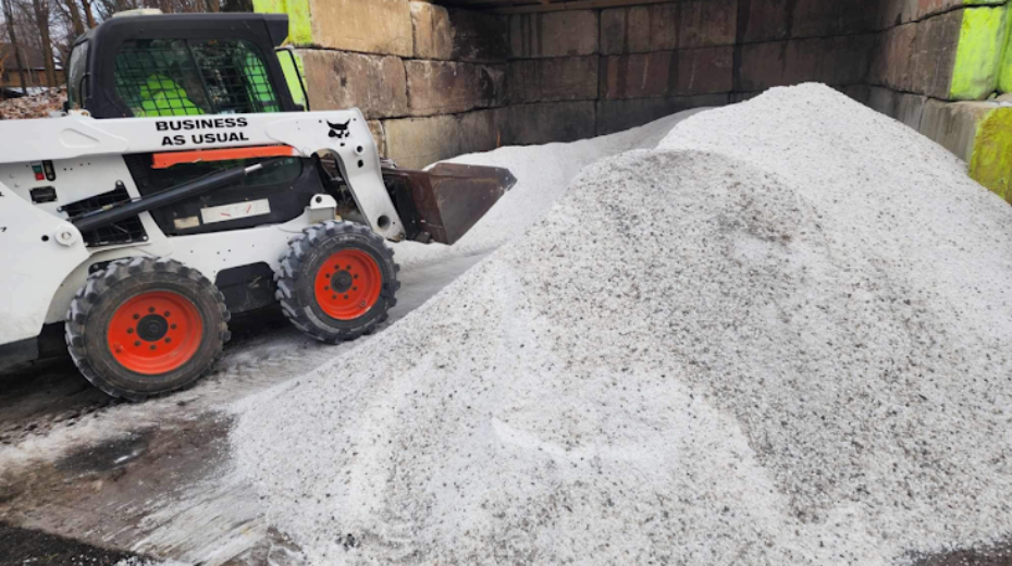 White Bobcat loader scoops up a pile of coarse, granular salt.