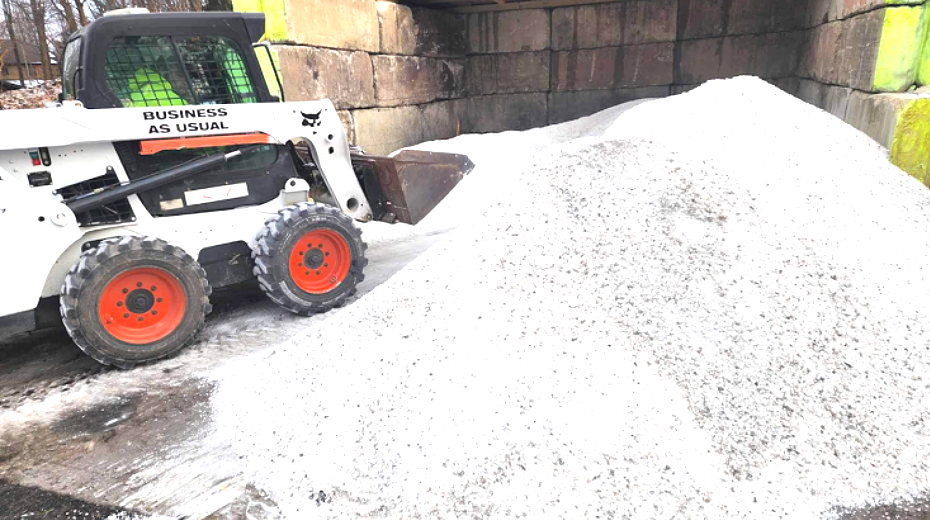 Bobcat loader scoops up a large pile of white salt, preparing it for distribution.
