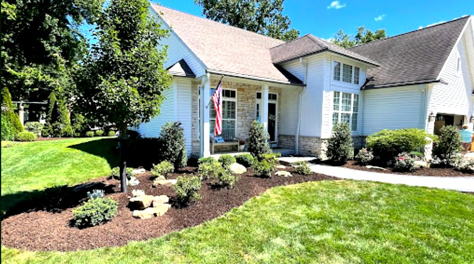 White house with stone accents, lush green lawn, and landscaped flower beds.