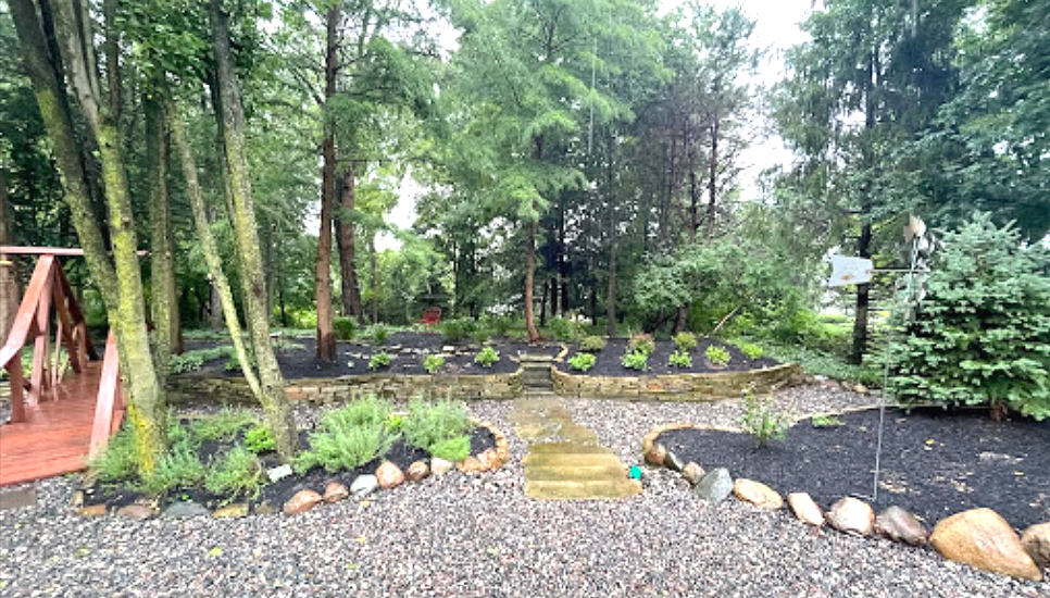 Garden with a stone path, flowerbeds, trees, and mulch, on an overcast day.