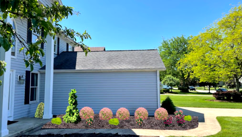 Landscaped house exterior with flower beds and a green lawn under a blue sky.