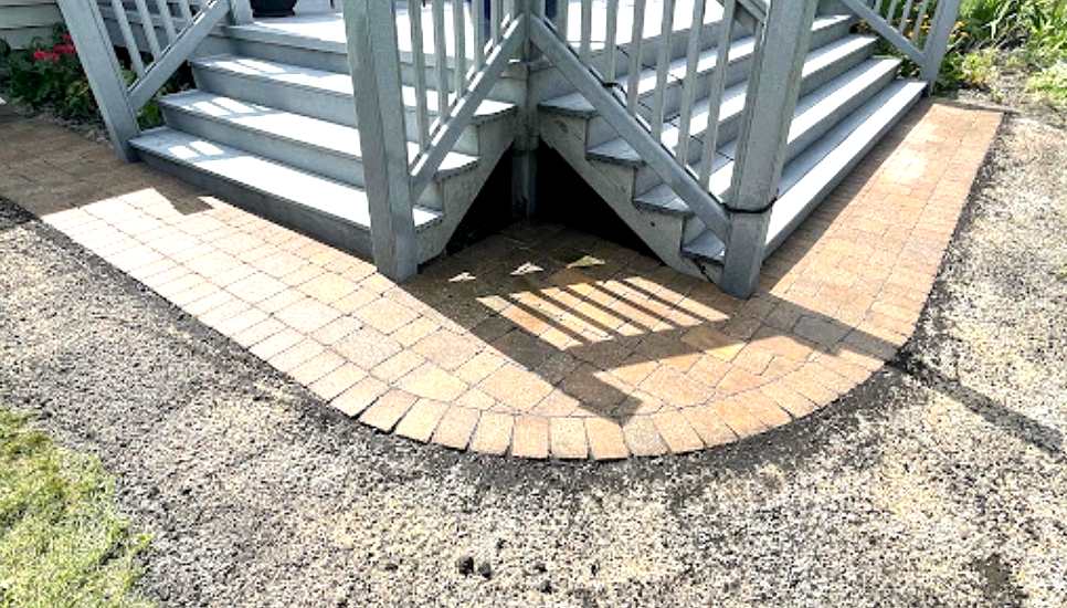 Brick pathway curving around gray wooden stairs leading to a deck.