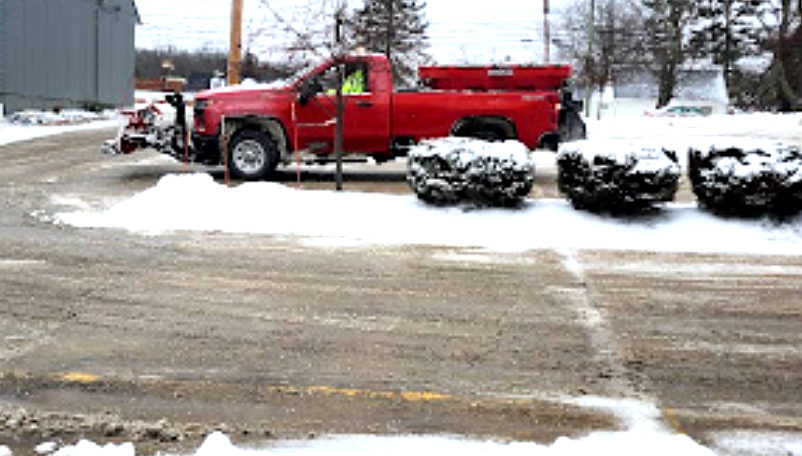 Red pickup truck with plow clearing snow from a paved road on a winter day.
