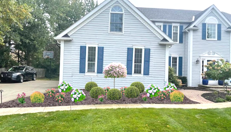 A two-story blue house with blue shutters and a flower bed in front.