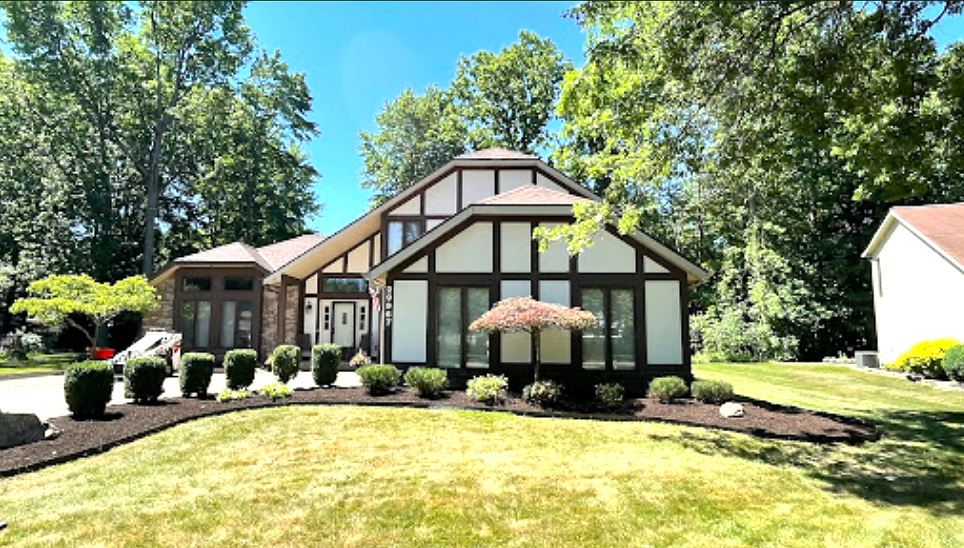 Tudor-style house with dark brown trim, white siding, and manicured landscaping under a blue sky.