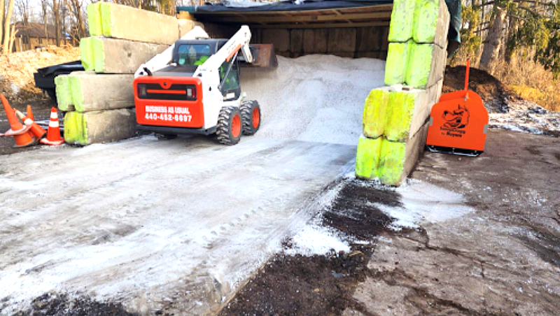 Bobcat loader moving white material inside a structure, surrounded by concrete barriers.