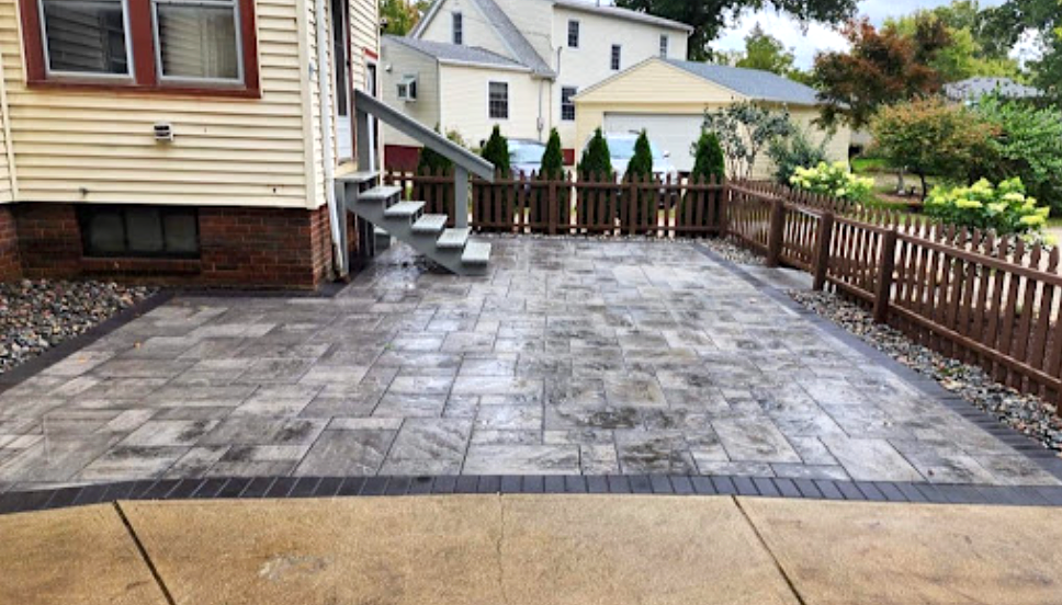 Patio with gray pavers, brown wooden fence and stairs. House in background.