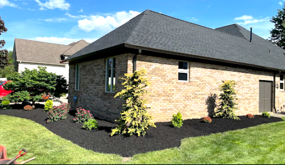 Brick house exterior with black mulch landscaping, green lawn, and blue sky.