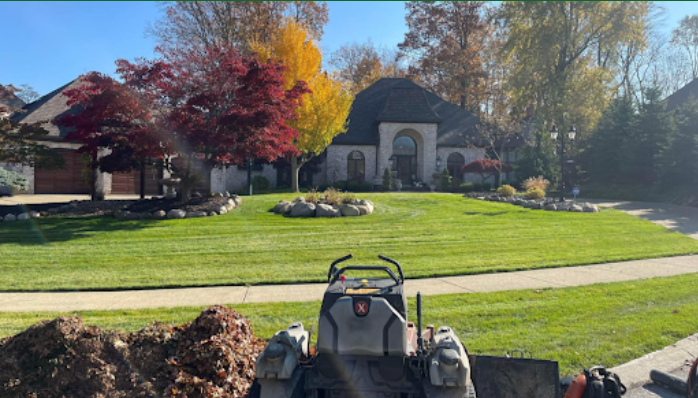 A tractor working on a lawn in front of a house with fall foliage.