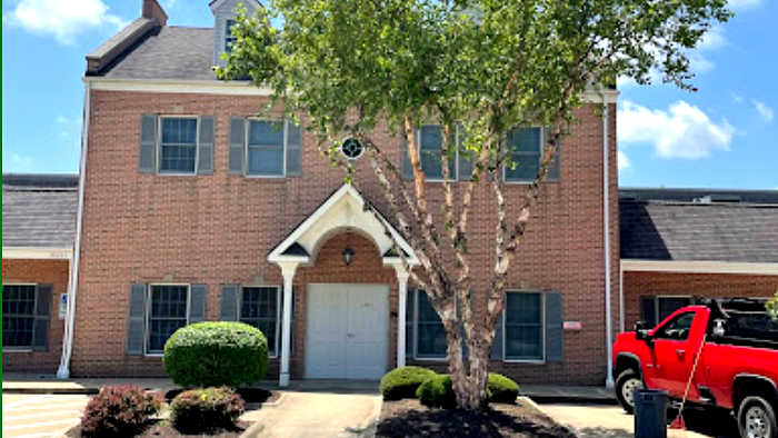 Brick building with gray shutters and tree in front; red truck on right.