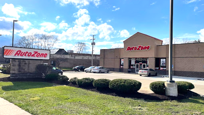 AutoZone store exterior with cars parked; green lawn, blue sky, and a sign.