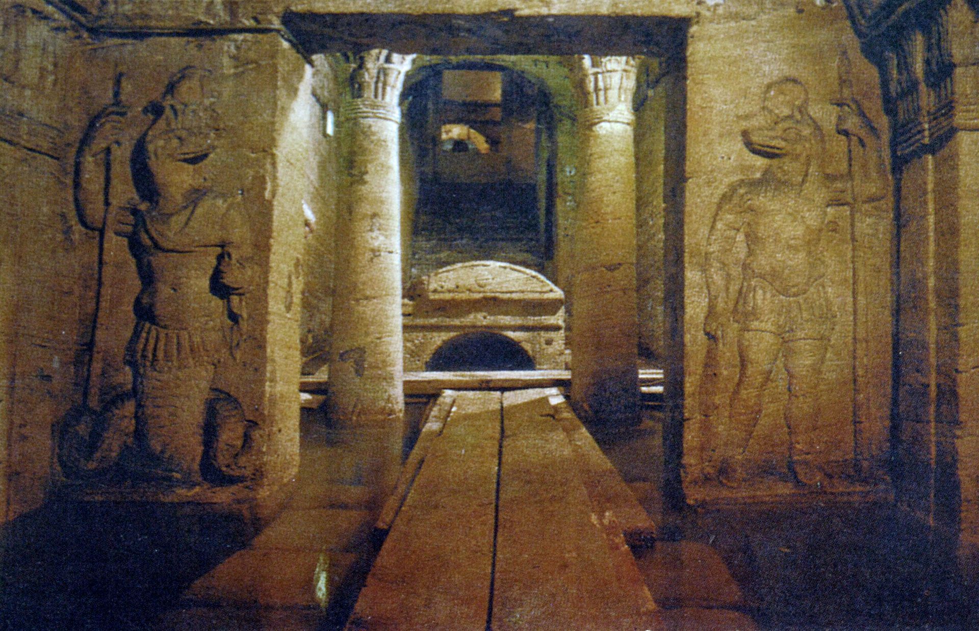 Ancient stone tomb interior with carvings and pillars.