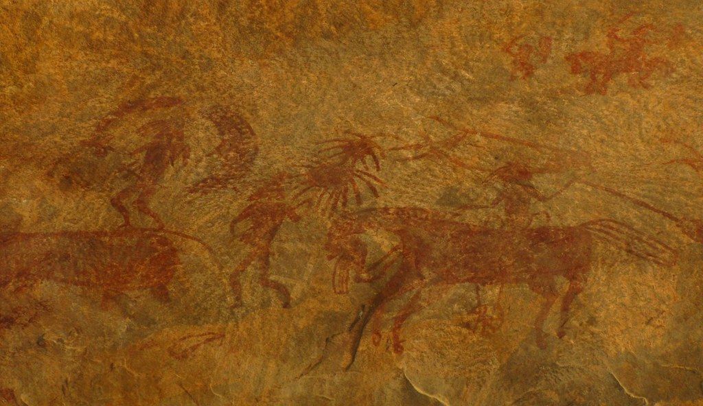 Cave painting of reddish-brown horses on a tan stone surface.