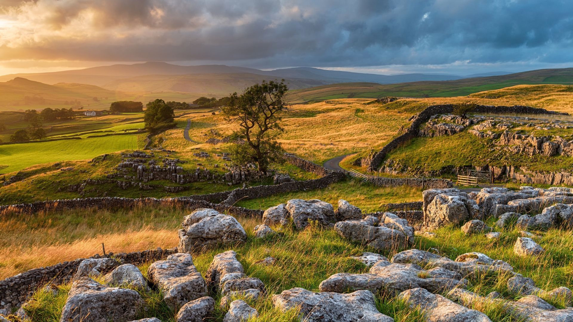 Rolling green hills with stone walls under a cloudy sky, illuminated by golden sunlight.