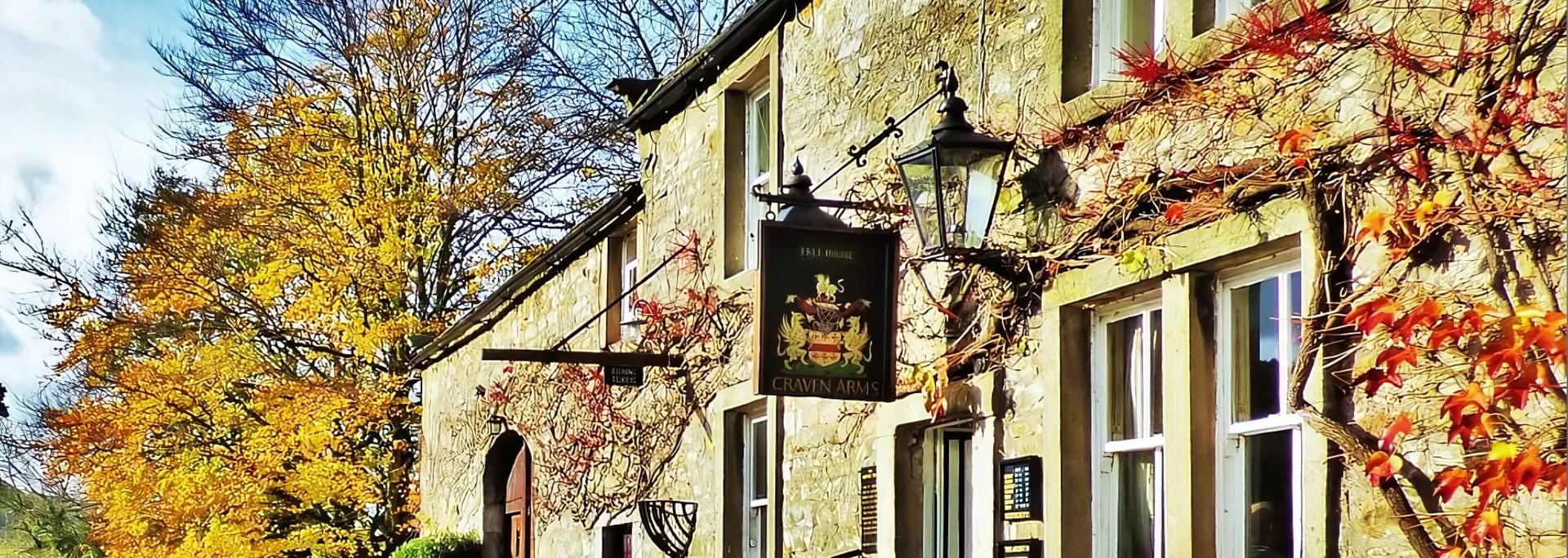 Stone building with a pub sign, windows, and autumn foliage.