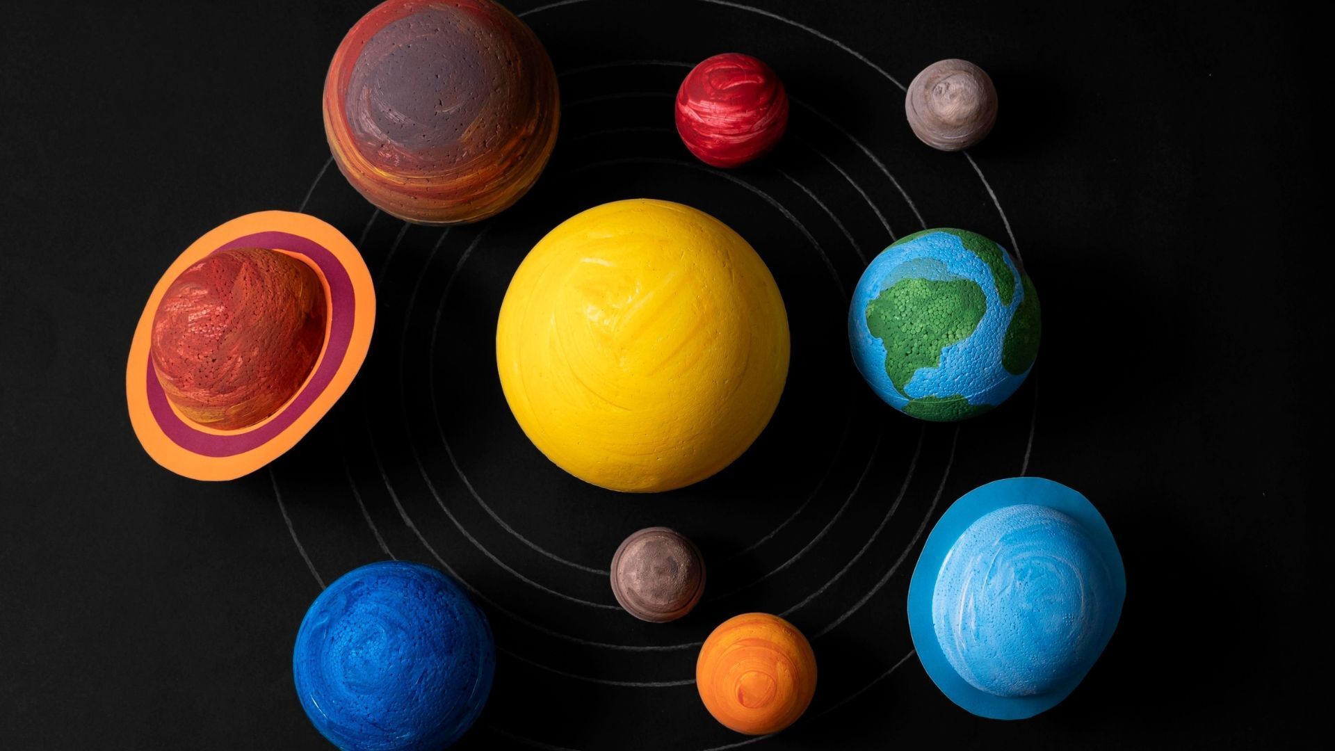Solar system model with yellow sun and colorful planets on black background.