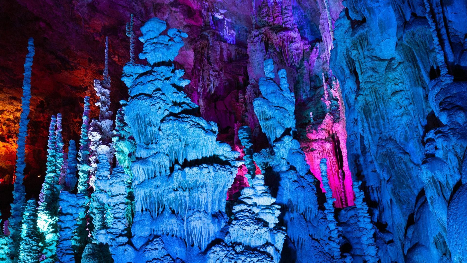 Colorful, illuminated cave formations; blue, purple, and red hues light up stalactites and stalagmites.