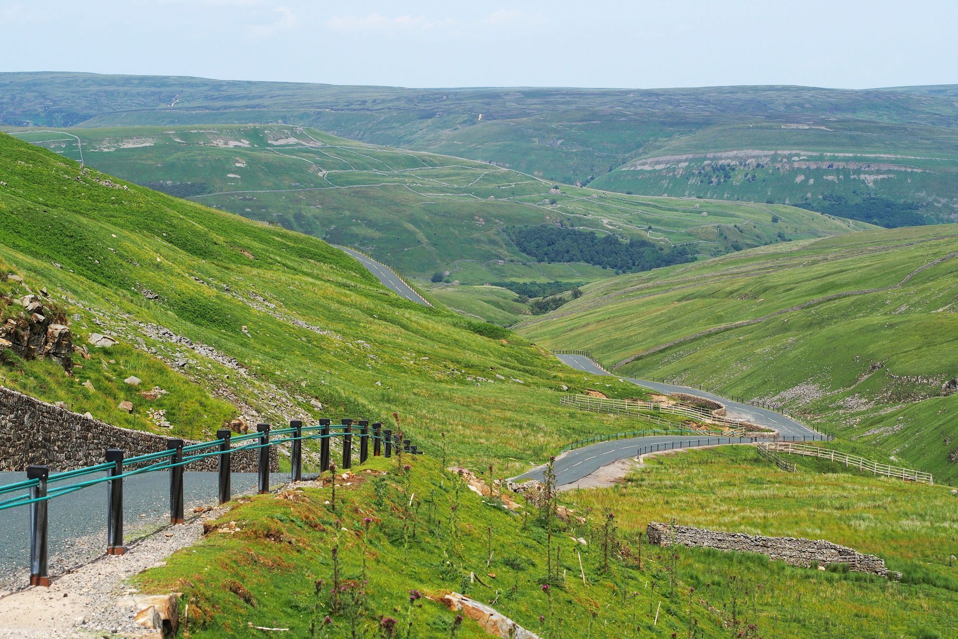 Winding road through lush green hills and valleys under a clear sky.