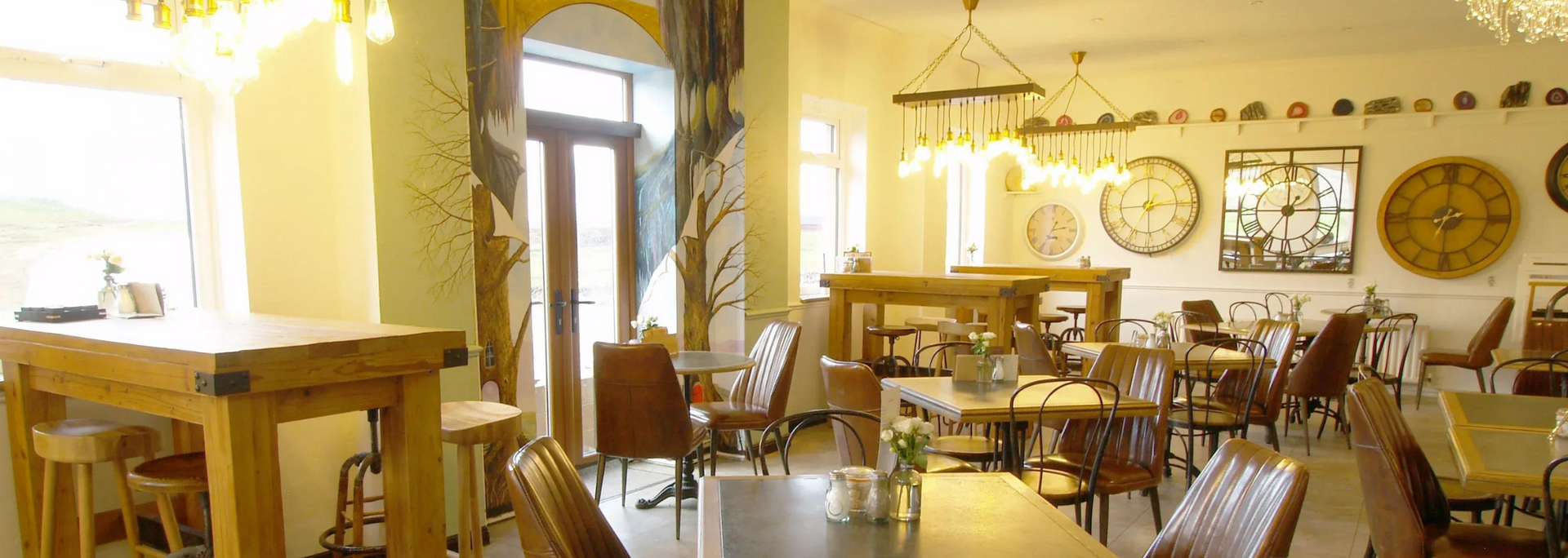 Restaurant interior with wooden tables, chairs, clocks on the wall, and decorative tree paintings.