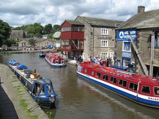 Boats on a canal in front of buildings, including a red structure. People stand on a boat.