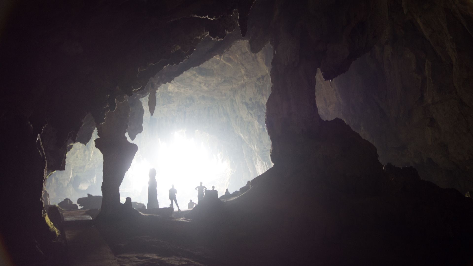 Bright light at cave exit, silhouetted stalagmites, and people.