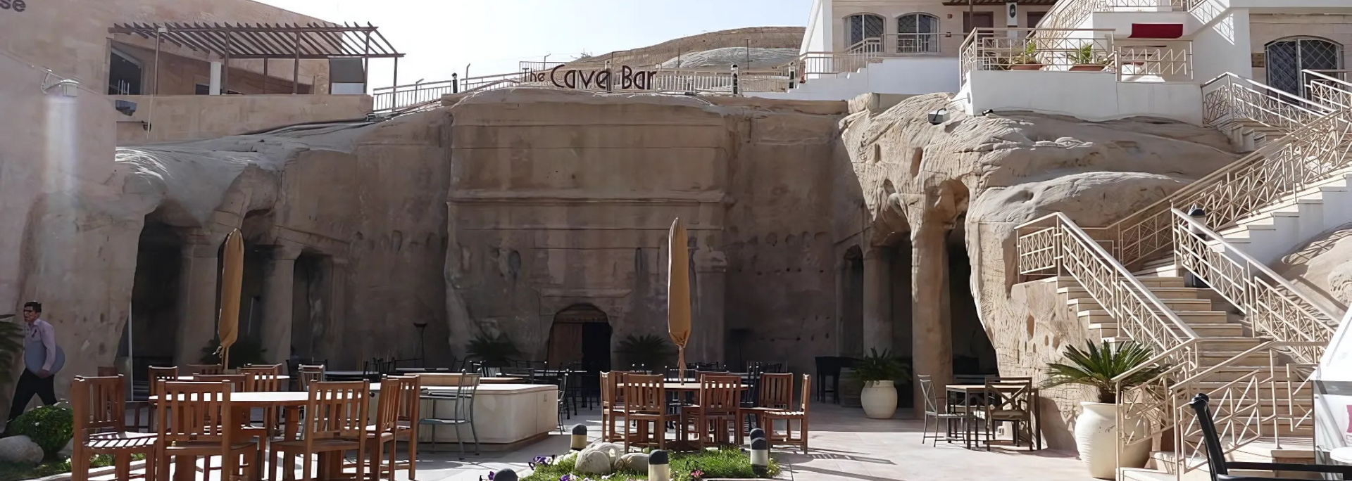 Outdoor courtyard with tables, carved stone walls, and stairs.